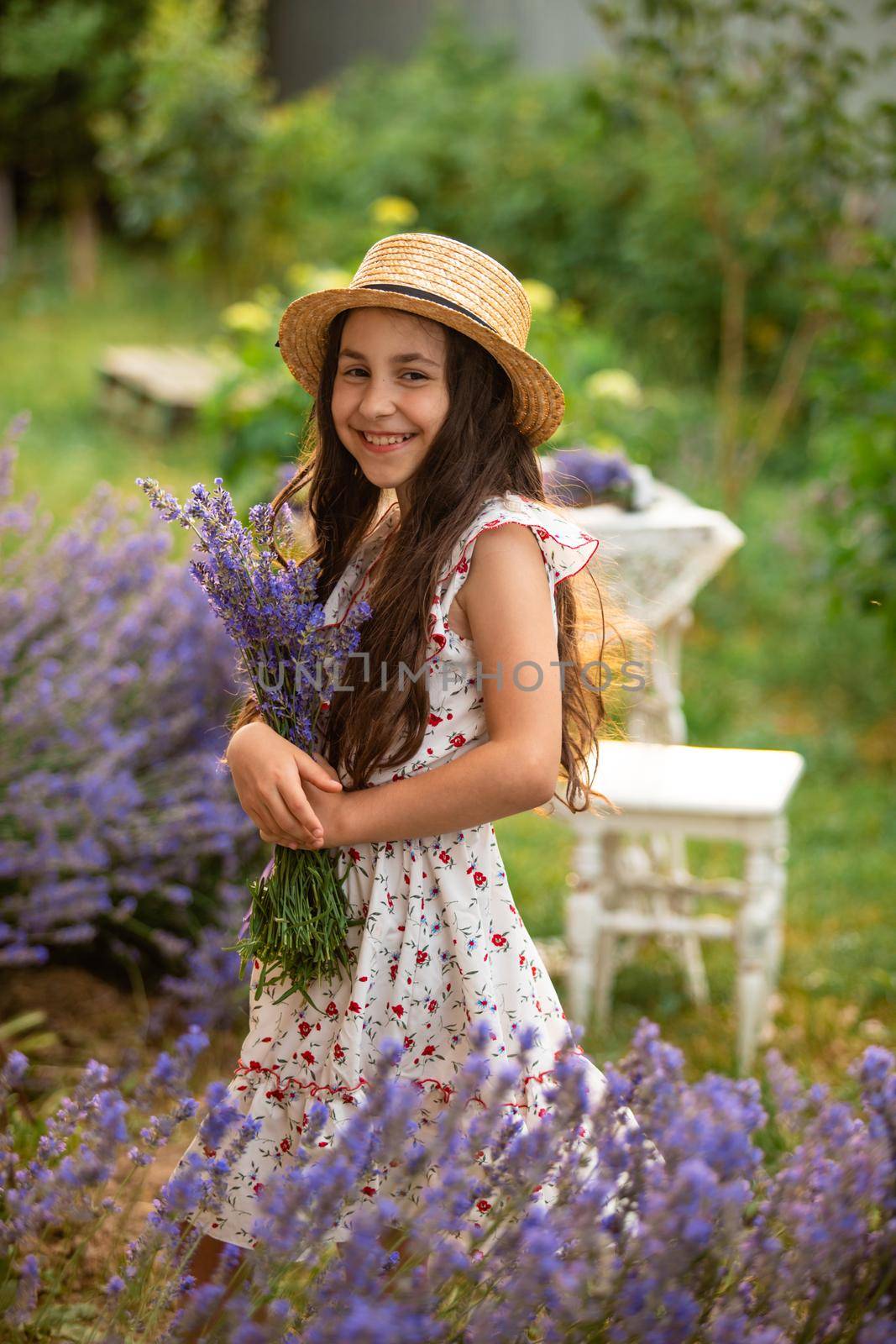 Beautiful long hair girl near lavender bushes at the garden. The girl is walking in the yard and collect flowers. A girl in a hat and dress.