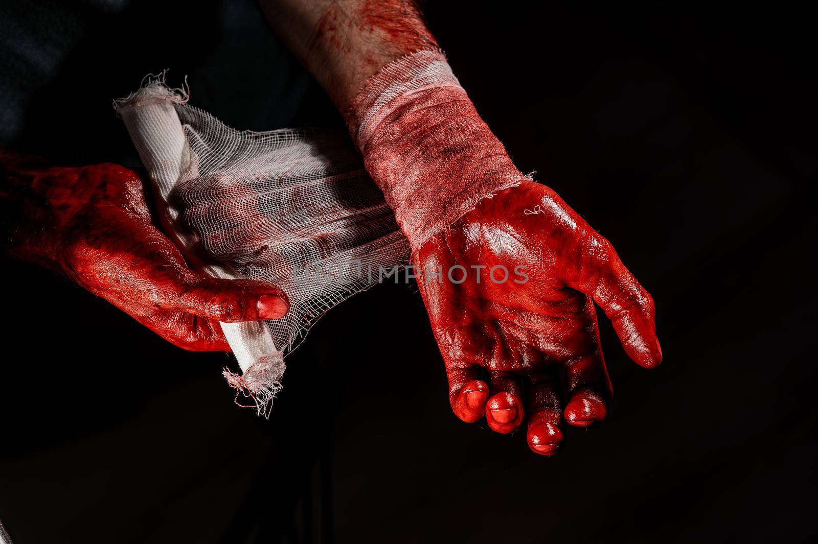 A man covered in blood bandages his hands