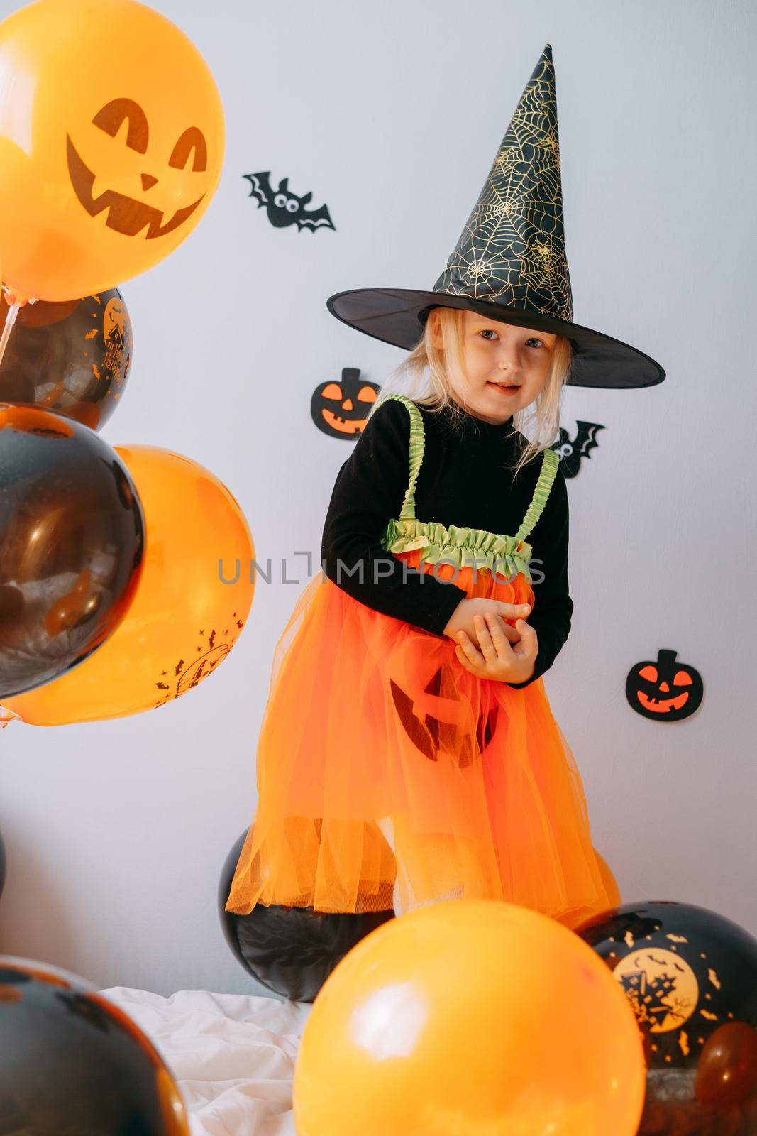 Children's Halloween - a girl in a witch hat and a carnival costume with airy orange and black balloons at home. Ready to celebrate Halloween by Annu1tochka