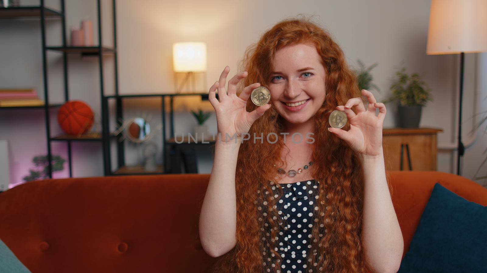 Woman freelancer holding two gold coins at home, successful developer programmer. Girl stock trader earning bitcoins after online monitoring trading operations. Increasing wealth, financial prosperity