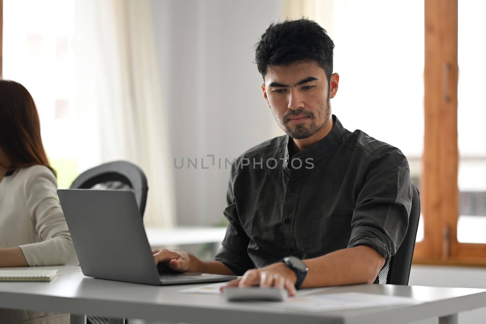 Handsome businessman working with laptop computer and using calculator at his office desk.