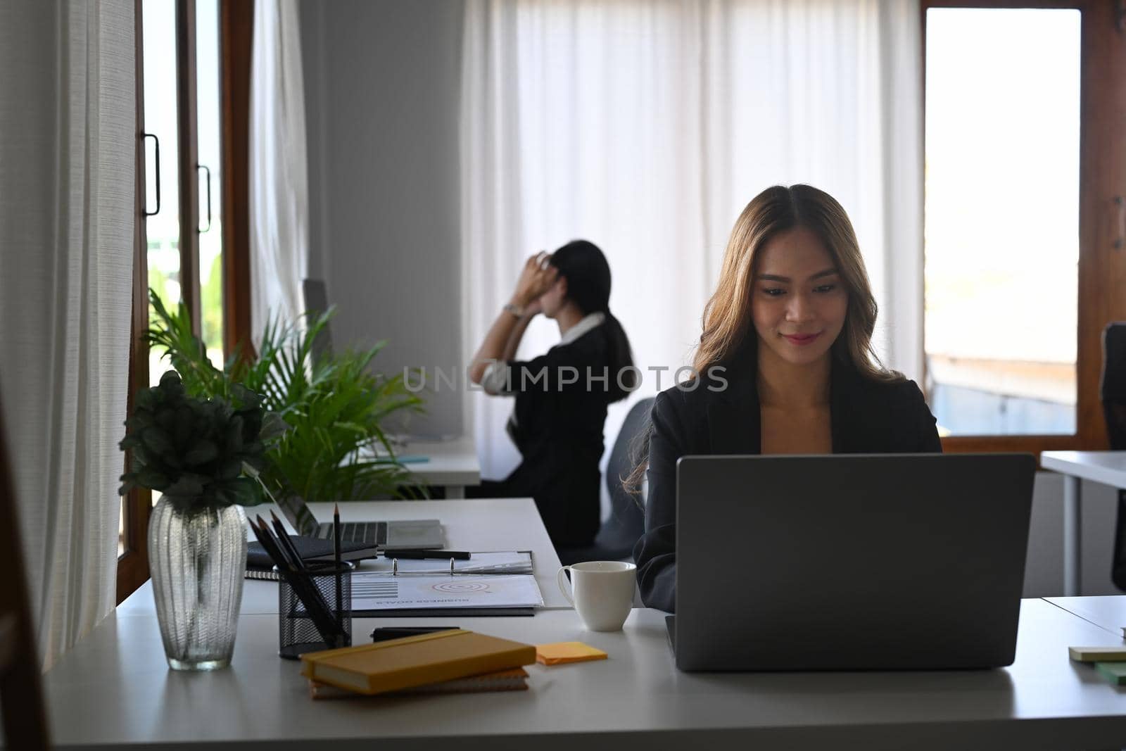 Young businesswoman working with laptop computer while sitting with her colleague in office.