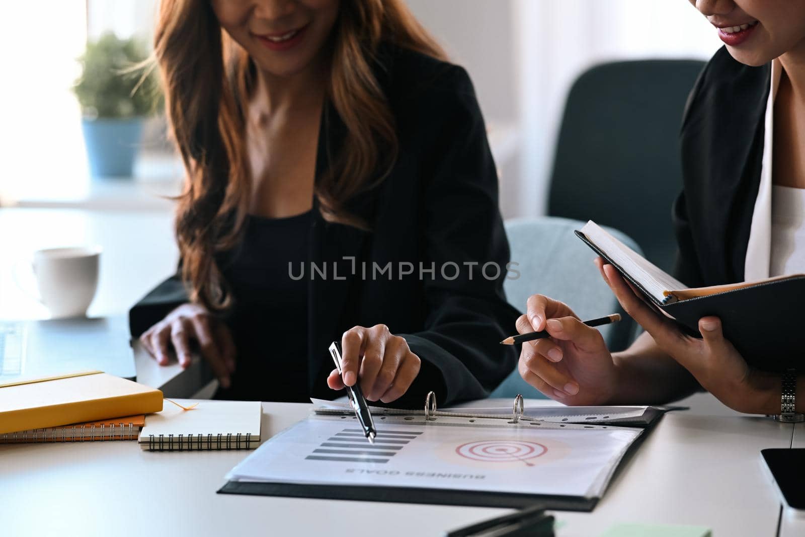 Two young business women analyzing financial graphs documents together in office.