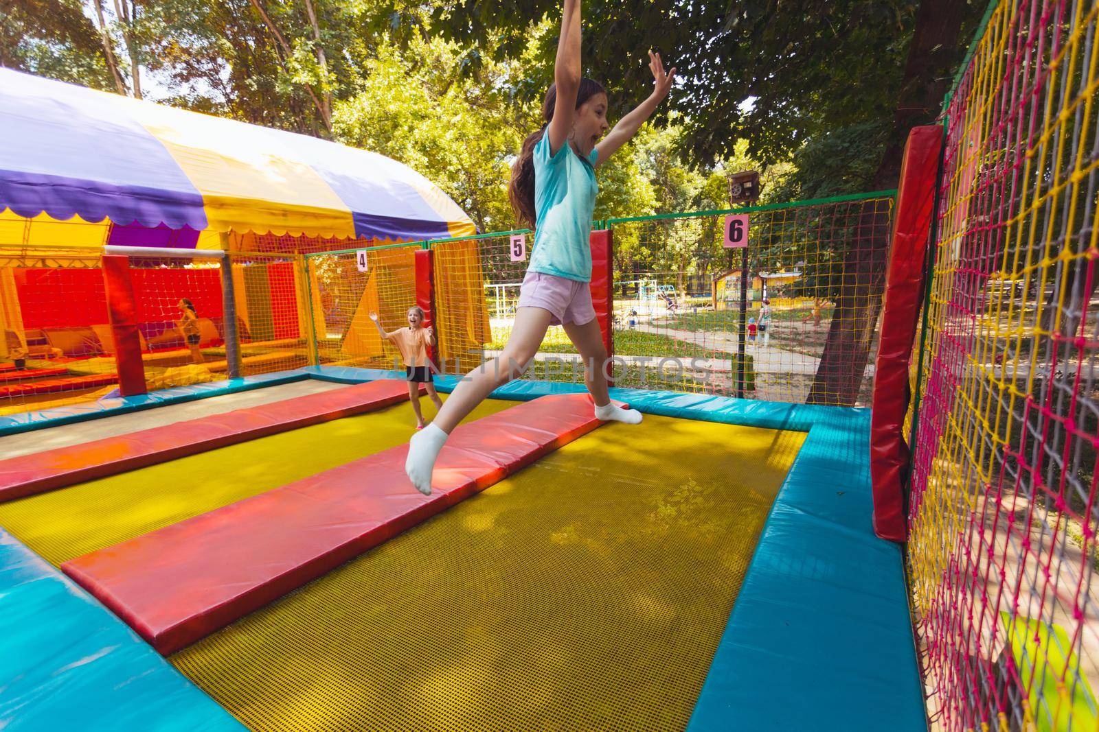 The young children are jumping in the bright trampoline park outdoors in the summer park