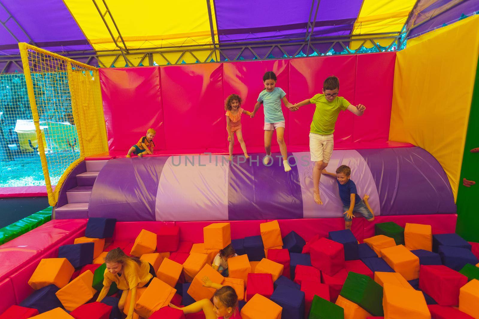 The happy little kids are jumping into dry pool with soft cubes. The group of children are playing in the trampoline park