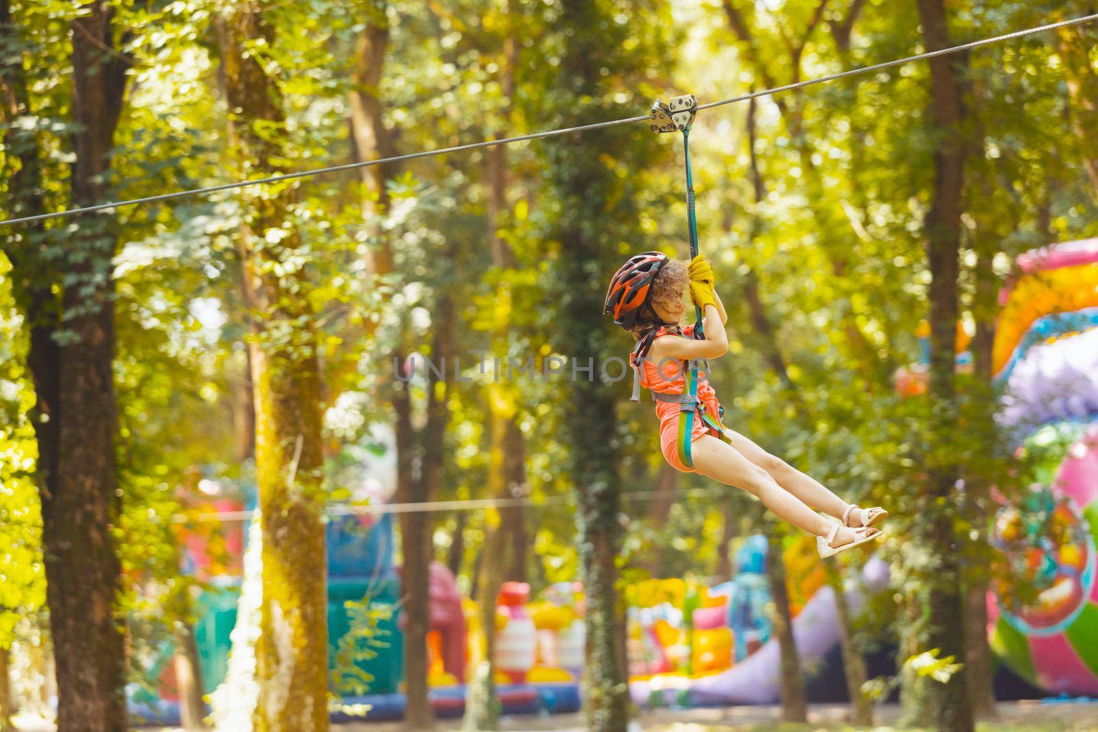 The little girl in a protective helmet goes down the zipline in the rope park