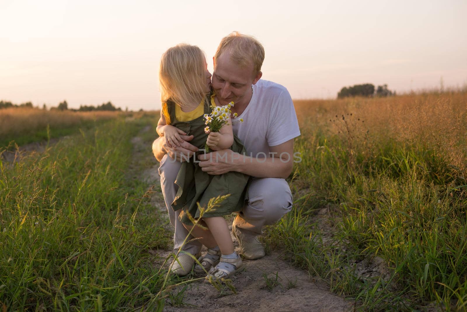 Dad and his blonde daughter are walking and having fun in a chamomile field. The concept of Father's Day, family and nature walks.