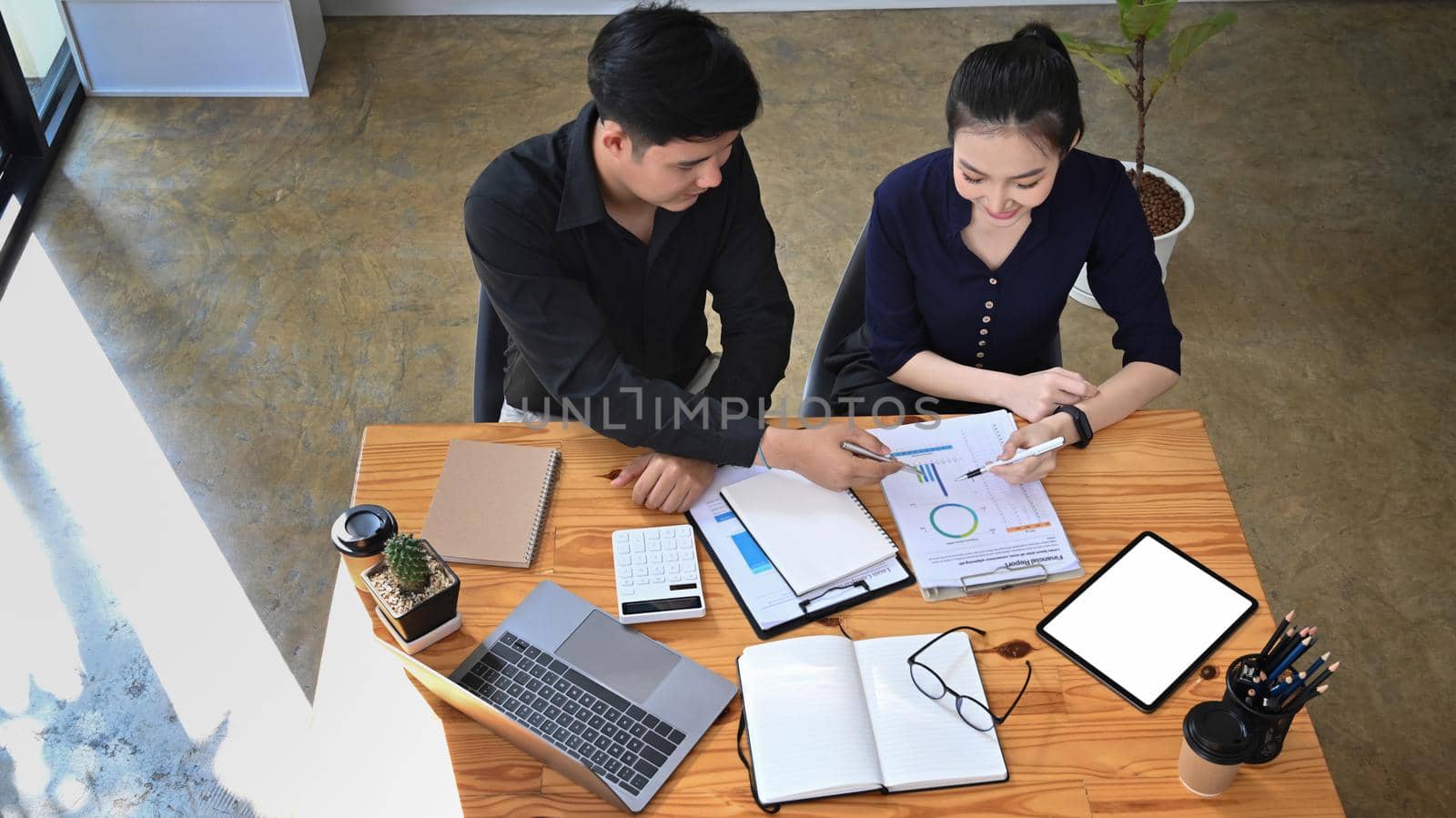 Above view two young business people working with financial graphs and statistics documents at office. by prathanchorruangsak