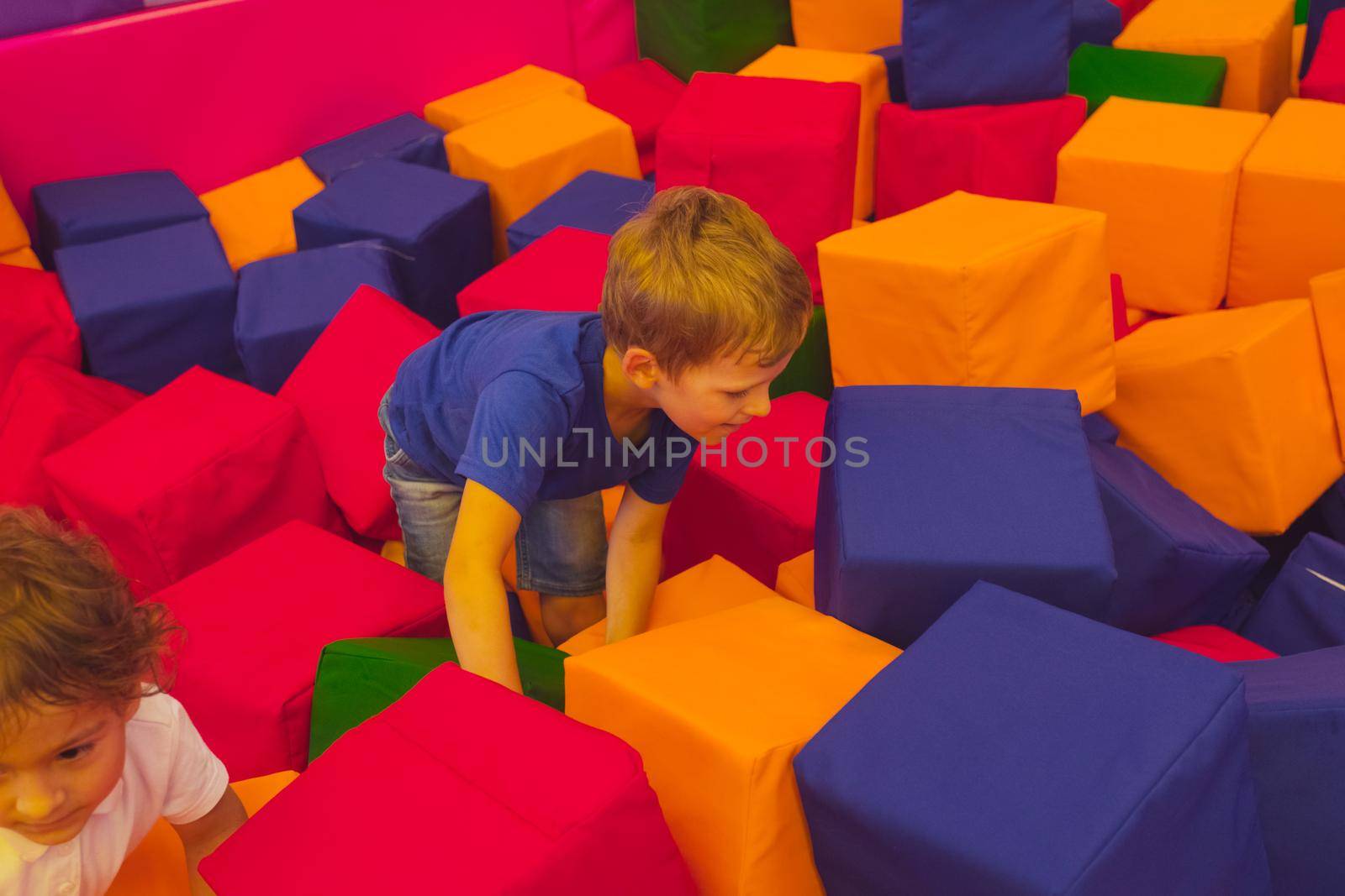 Portrait of the cute toddler boy who is standing in the playroom among soft cubes and looking at the camera