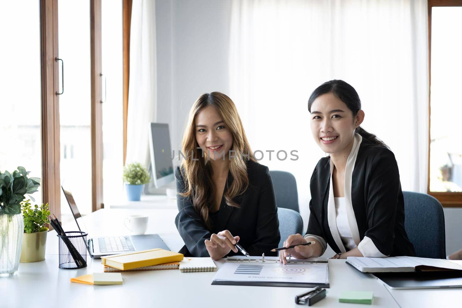 Two confident businesswoman sitting together in office and smiling to camera.