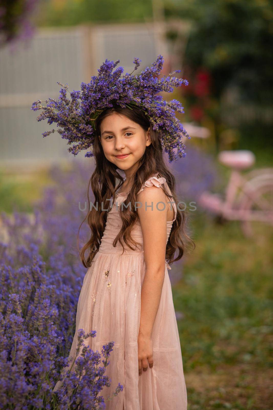 Beautiful long hair girl near lavender bushes at the garden. The girl made a wreath from the flowers