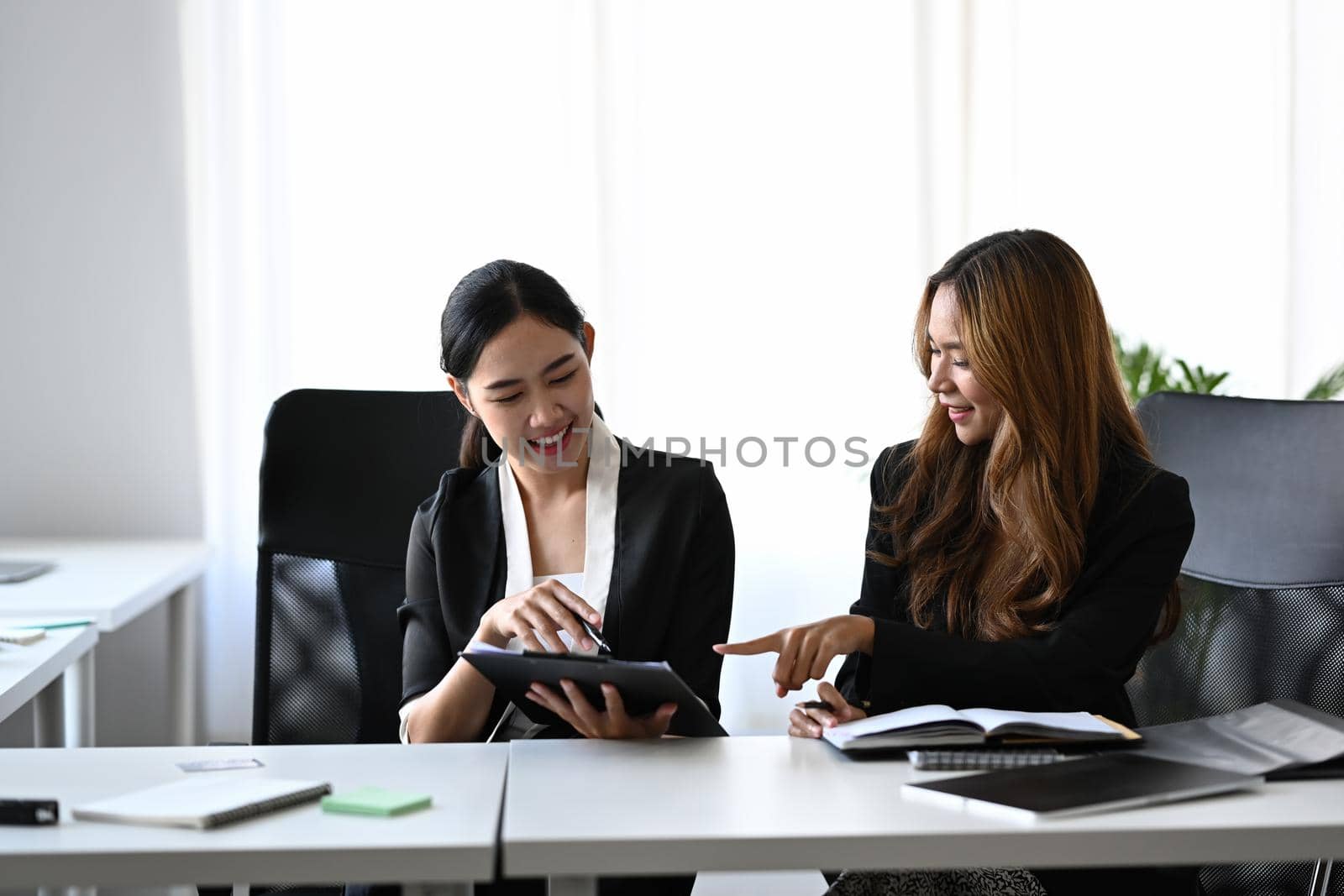 Two cheerful business women working on project together in modern workplace. by prathanchorruangsak