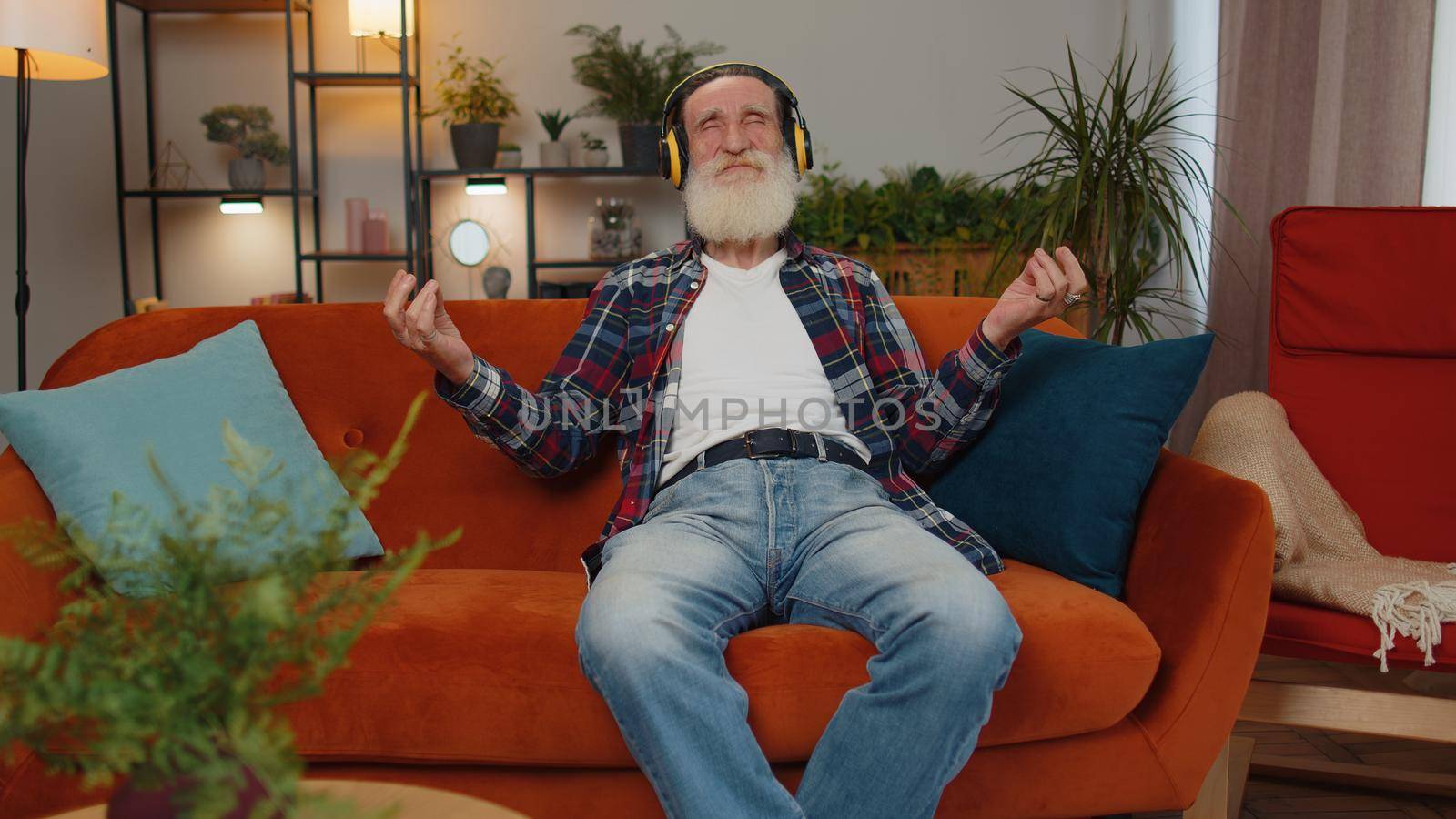 Keep calm down, relax, inner balance. Senior old grandfather man breathes deeply with mudra gesture eyes closed meditating with concentrated thoughts, peaceful mind sit at home in living room on couch