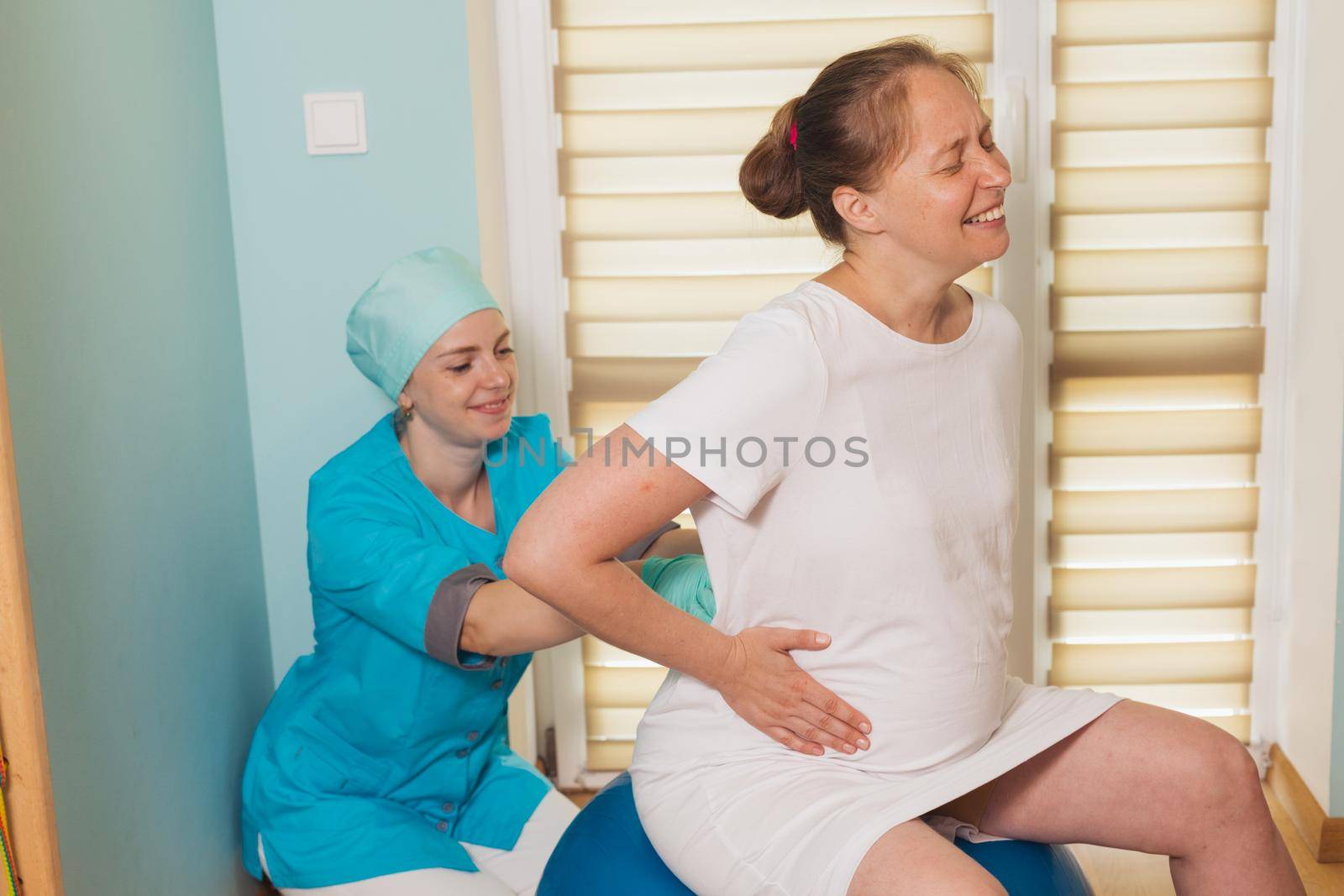 Woman gives birth at hospital, have a contraction on fitball. Nurse doing massage for woman in labor