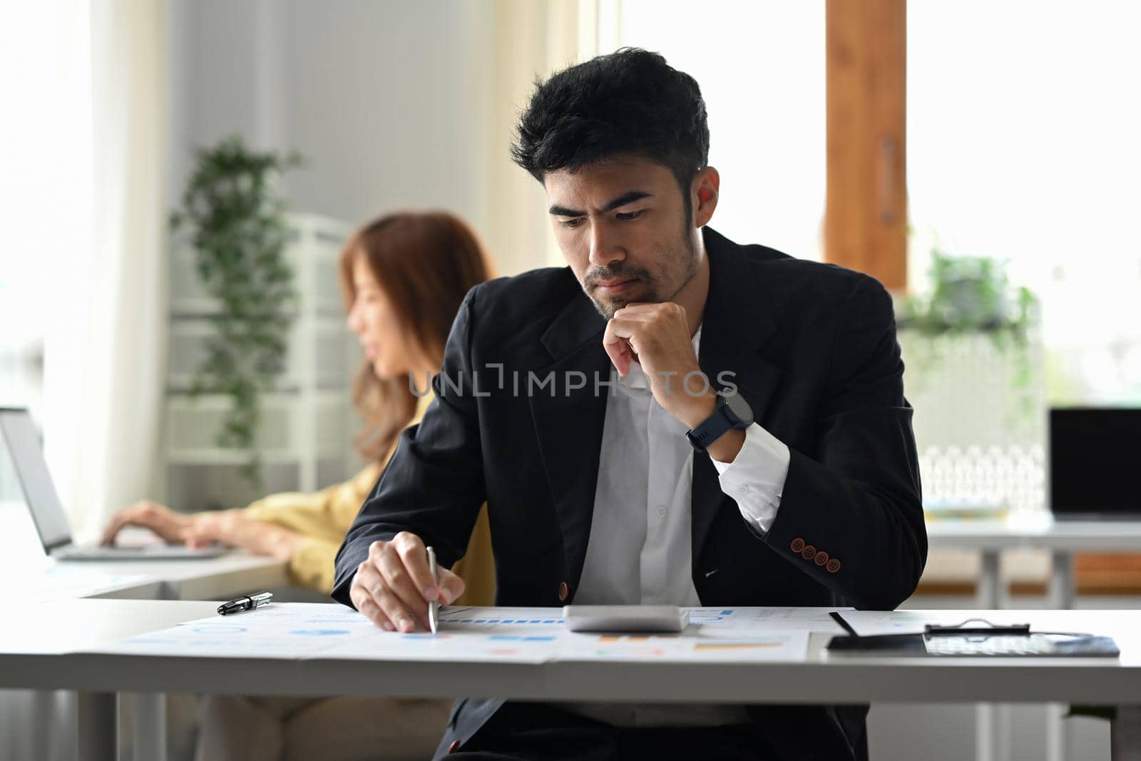 Focused male manager checking financial reports and using calculator at corporate office by prathanchorruangsak