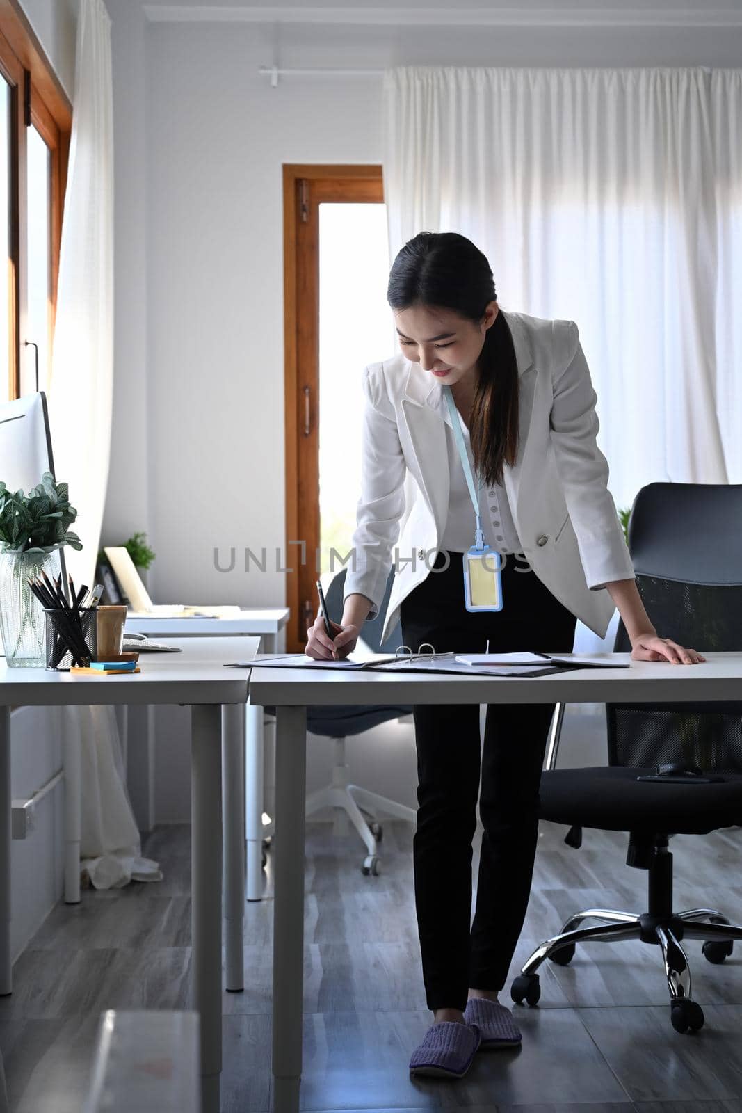 Full length portrait of businesswoman standing at her workplace and signing on business document. by prathanchorruangsak