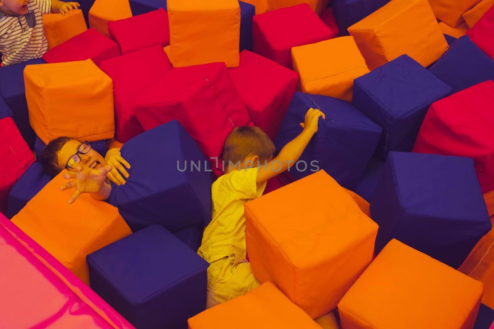 The children are playing with soft cubes in the dry pool. The children of all ages rest in the trampoline park