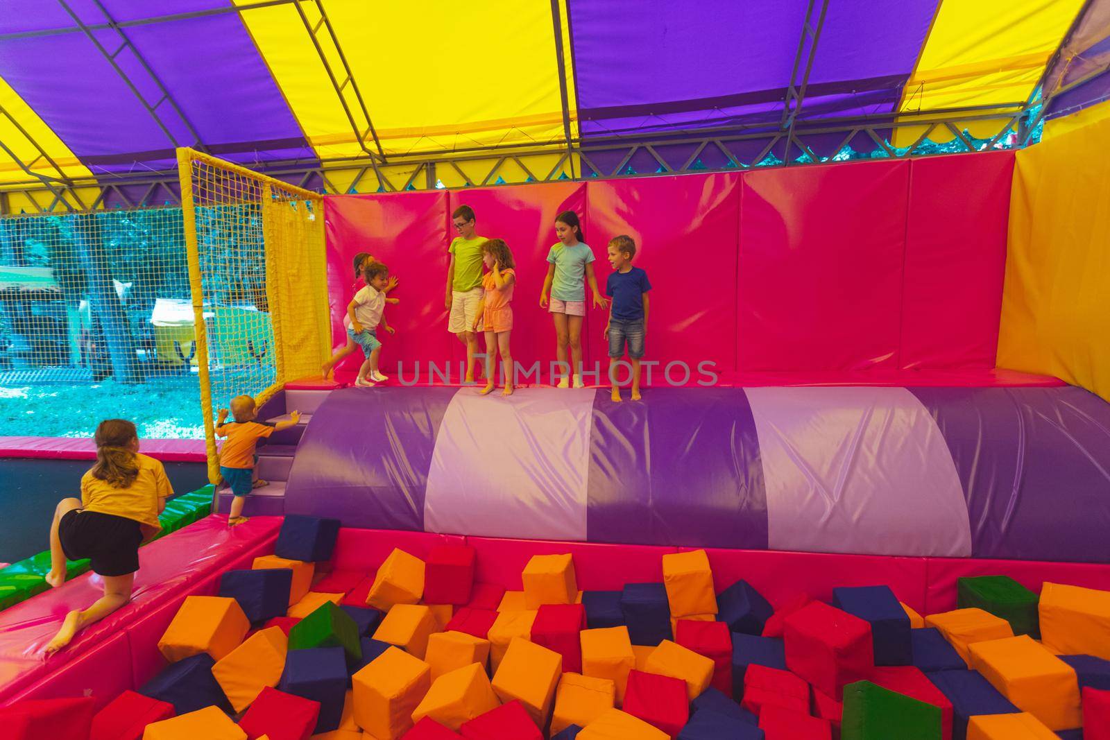 The happy little kids are jumping into dry pool with soft cubes. The group of children are playing in the trampoline park