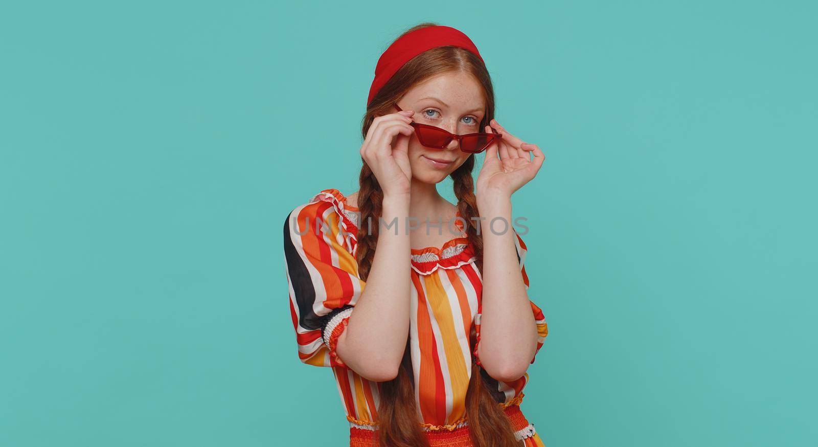 Portrait of seductive cheerful stylish girl wearing sunglasses, charming smile. People emotions concept. Young lovely redhead ginger teenager child posing isolated alone on blue studio background