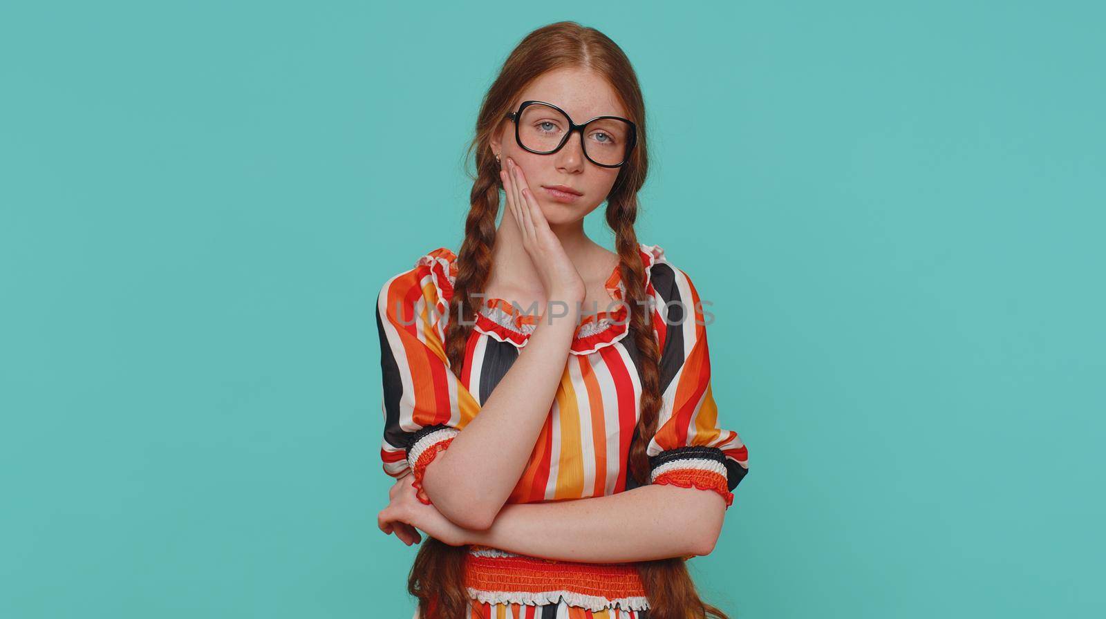 Redhead young girl touching sore cheek suffering from toothache cavities or gingivitis waiting for dentist appointment gums disease. Ginger teenager child studio shot isolated alone on blue background