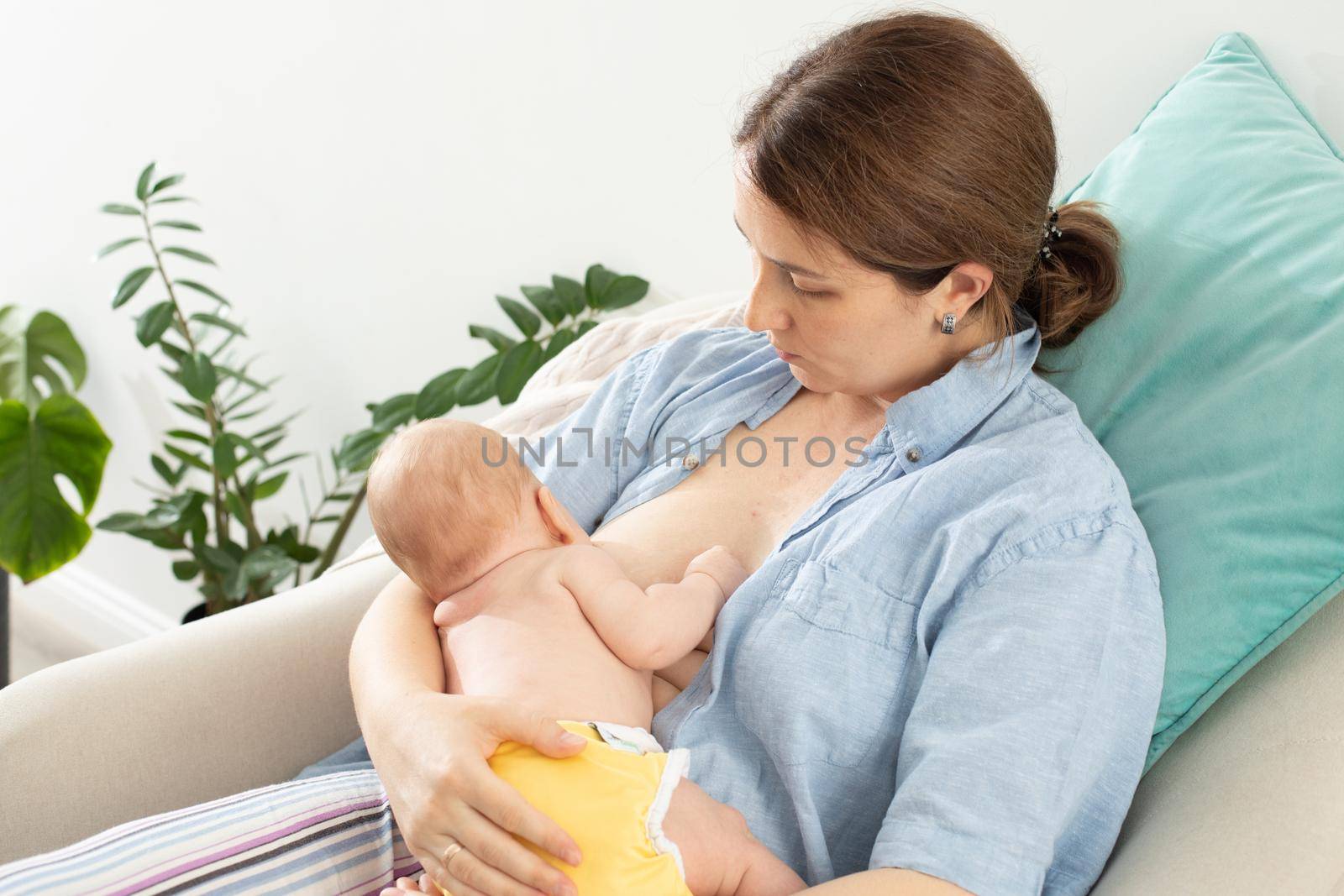 Mom holds her newborn baby in her arms. Mom rests in a chair during comfort breastfeeding