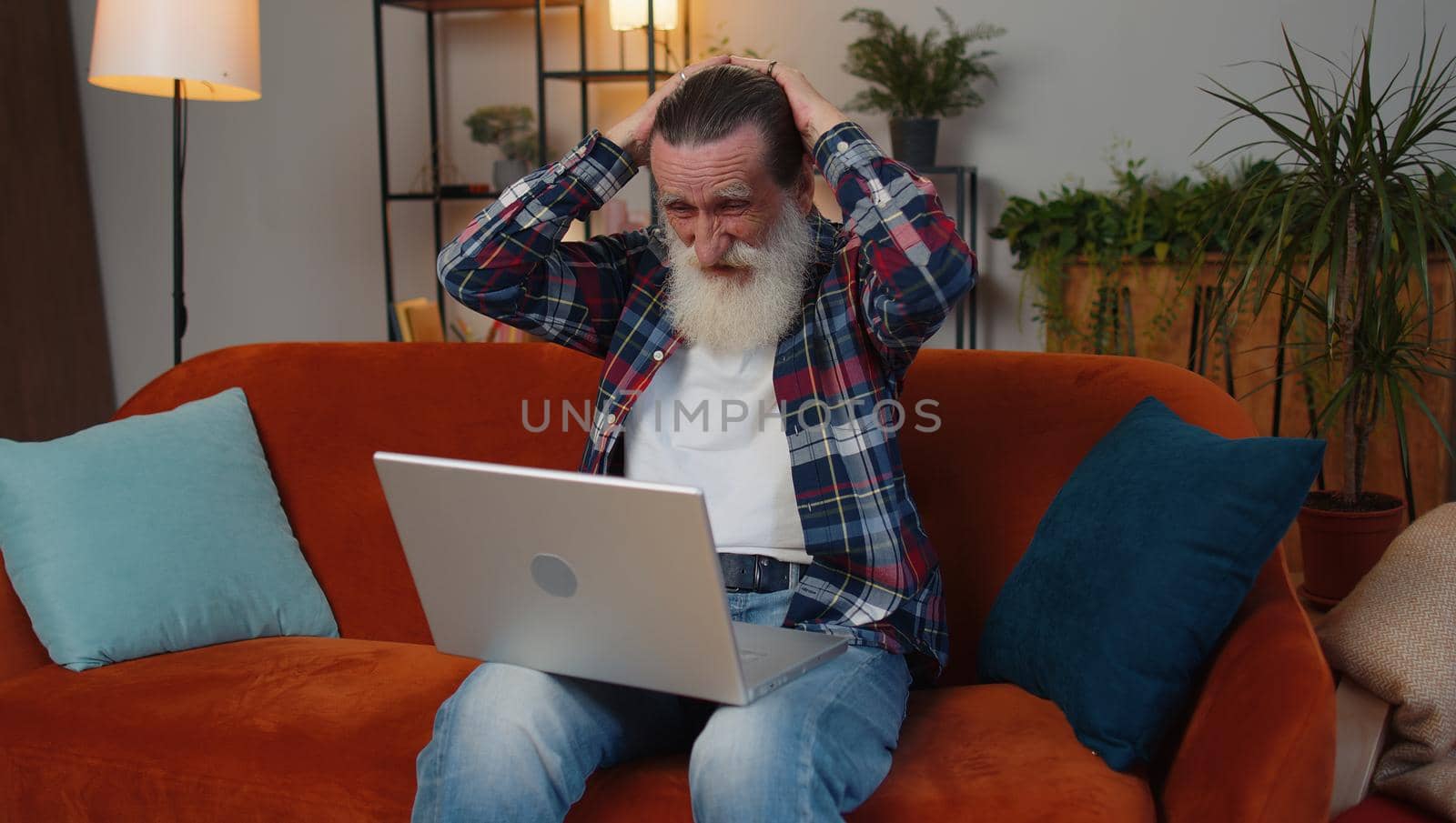 Sad senior old grandfather man use laptop typing browsing working, loses becoming surprised sudden lottery results, bad news, fortune loss, fail. Elderly retired pensioner at home living room couch