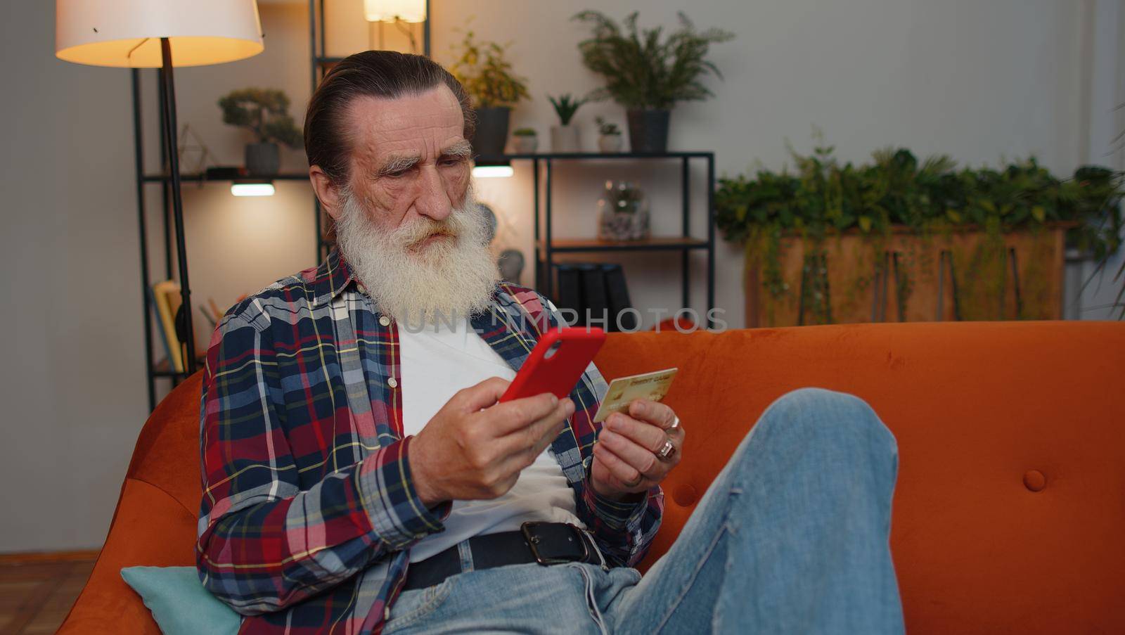 Happy shopaholic consumer senior old grandfather man sitting at home making online order food delivery, payment with credit plastic bank card. Discount sale on internet. Elderly retired pensioner guy