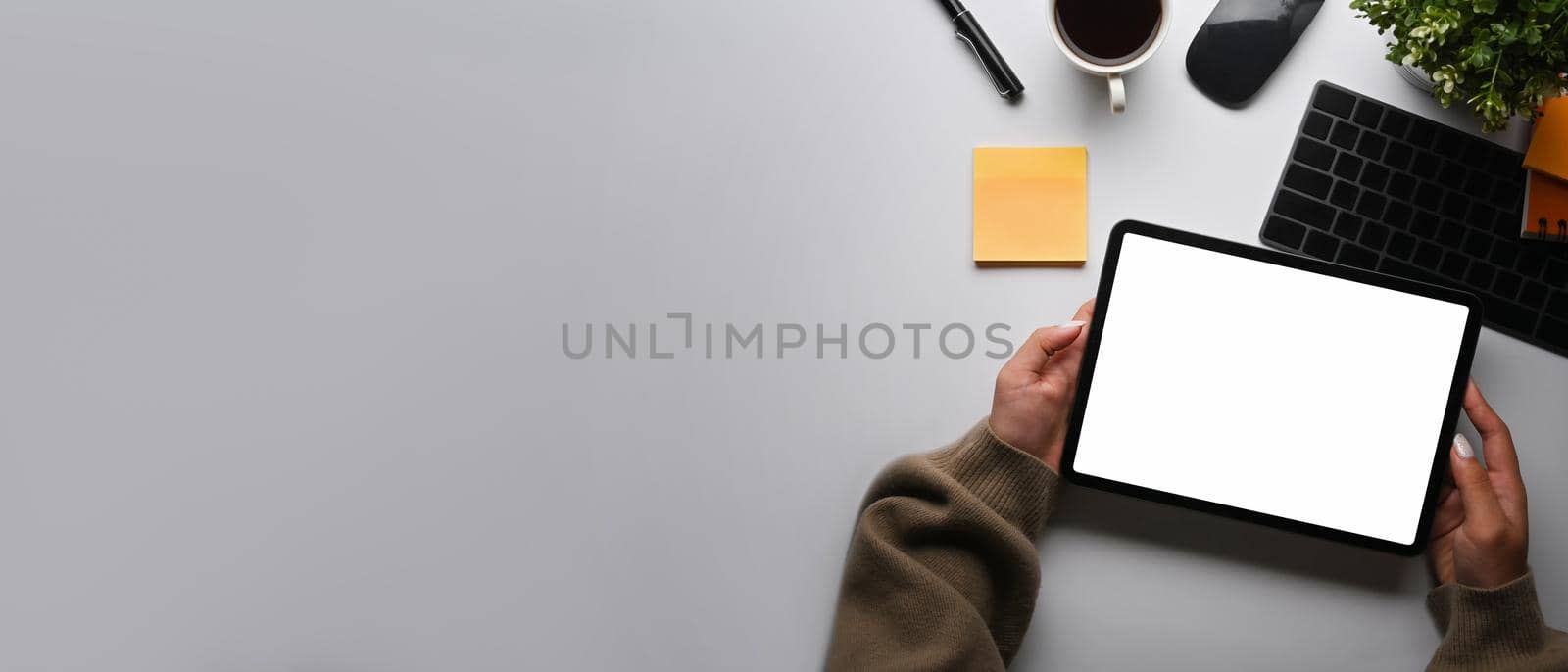 Overhead view creative woman holding digital tablet with empty screen on white table.