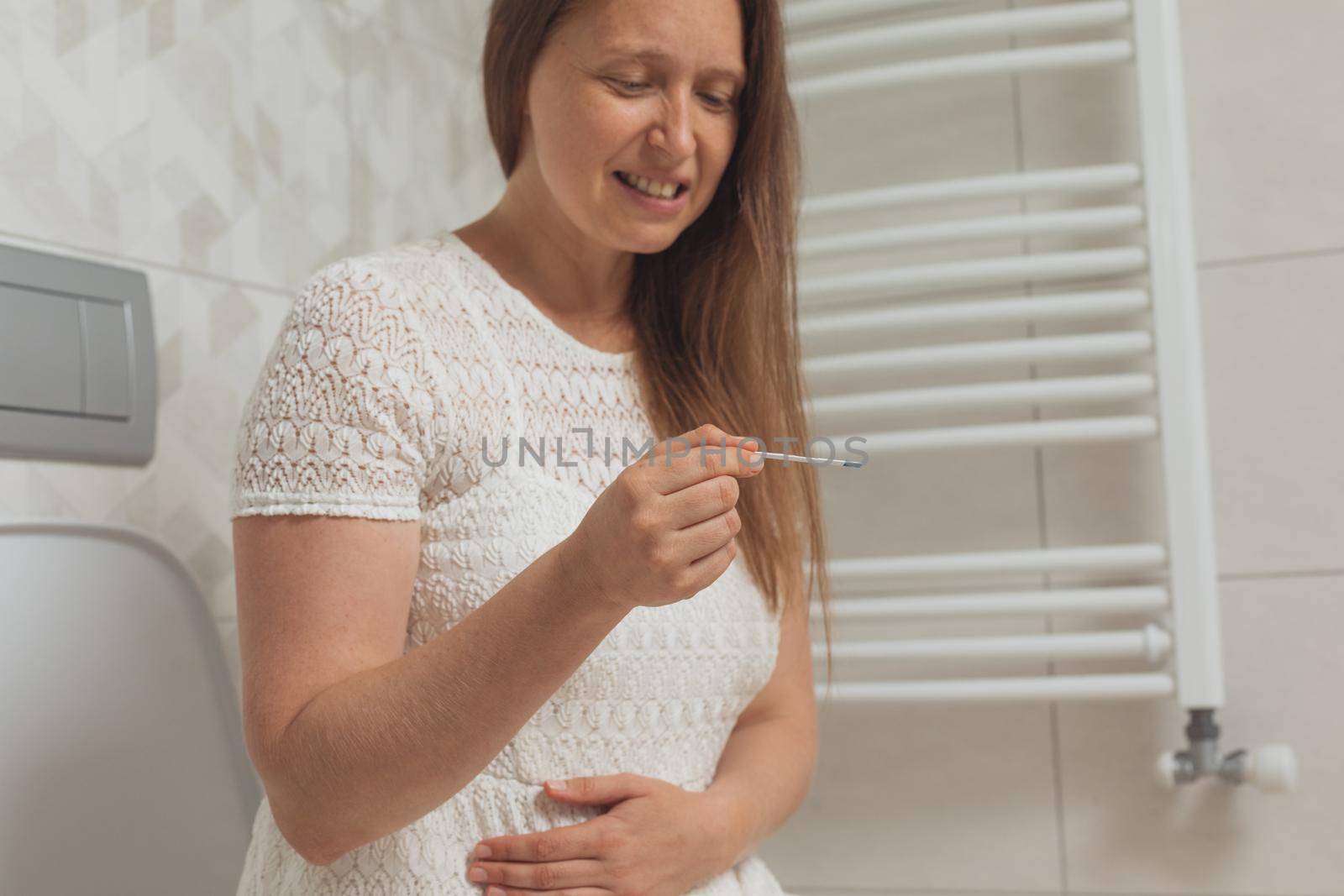 Confused middle age woman with pregnancy test in restroom