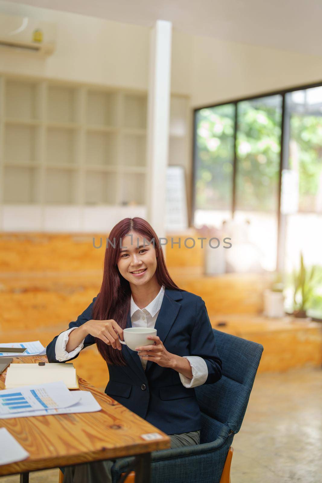 Asian female worker using computer and budget documents on desk.