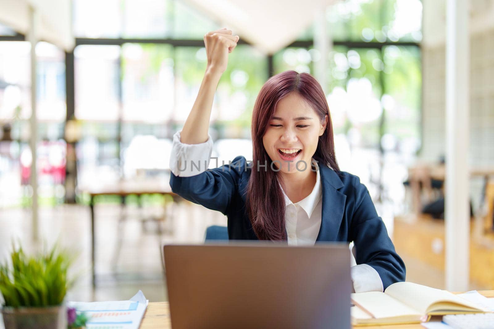 cheerful Asian celebrating her victory online with her laptop.