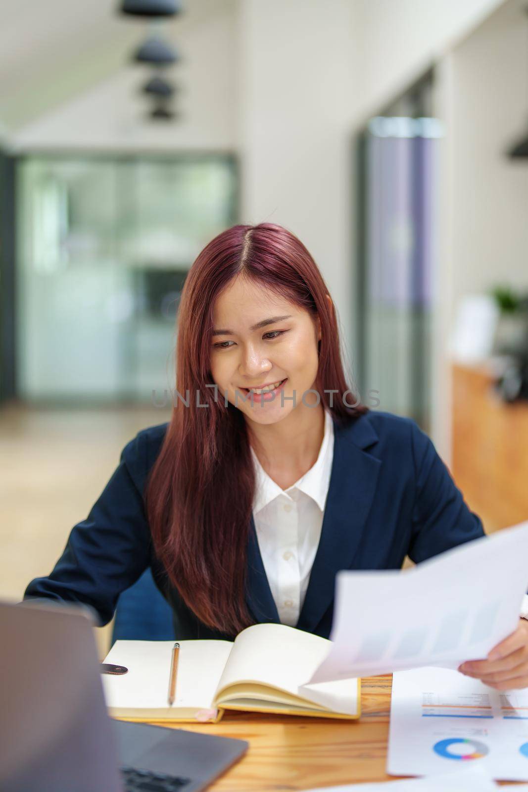 Asian female worker using computer and budget documents on desk.