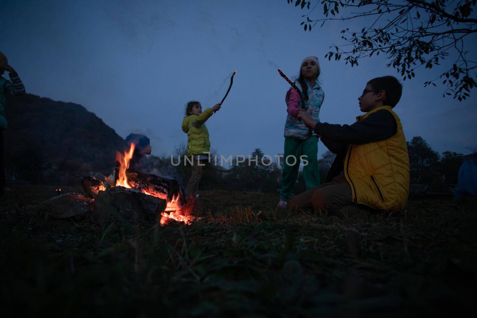 Children after hiking have a picnic - group of happy friends frying sausages on campfire