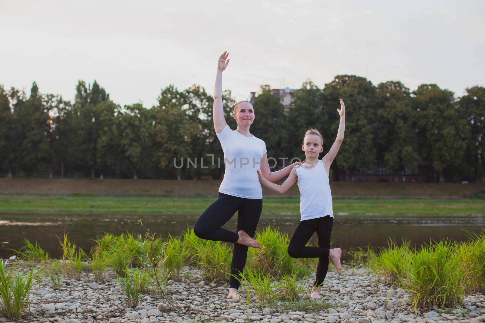 Son and mother are doing exercises in the park near river