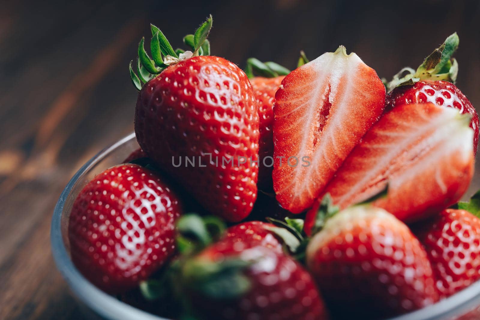 Fresh strawberries in a glass bowl on wooden background in rustic style, healthy sweet food, vitamins and fruity concept. Selective focus