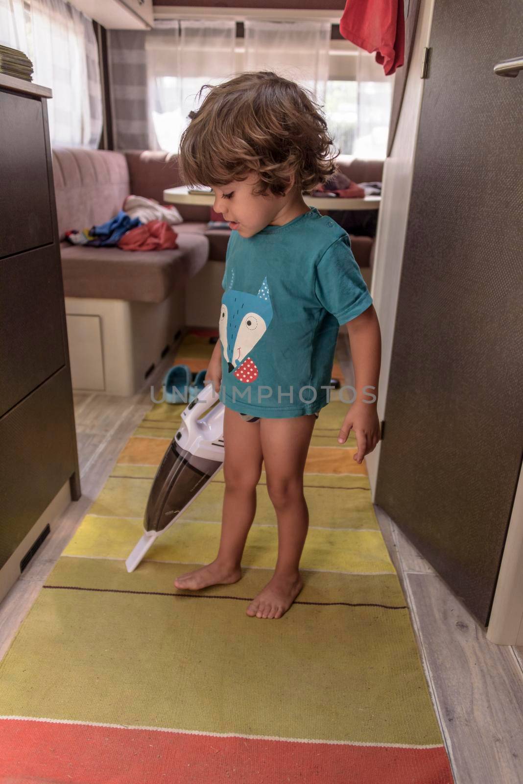 A sweet little boy vacuums the caravan while on vacation. A cute boy is cleaning the caravan