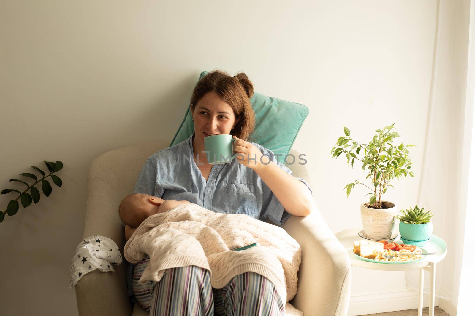 Woman drink tea or coffee during process of breastfeeding of newborn baby by oksix