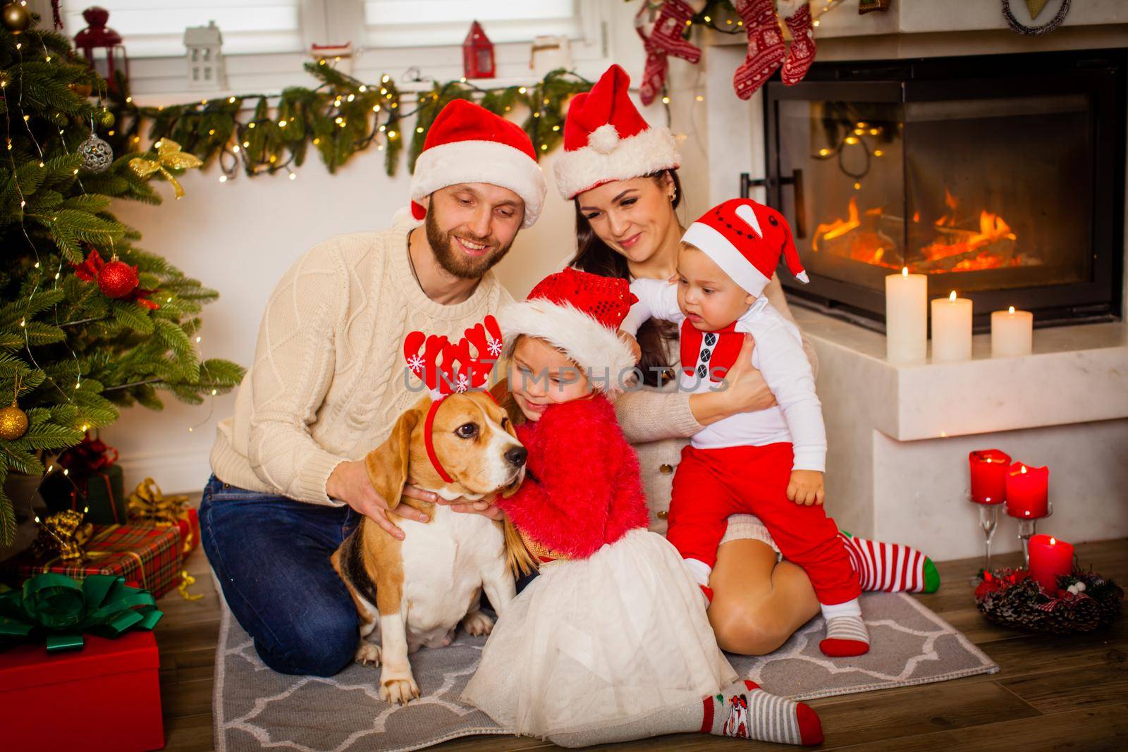 Happy family with dog beagle are waiting for the Christmas in Santa Claus hats while sitting near beautiful Christmas tree at home.