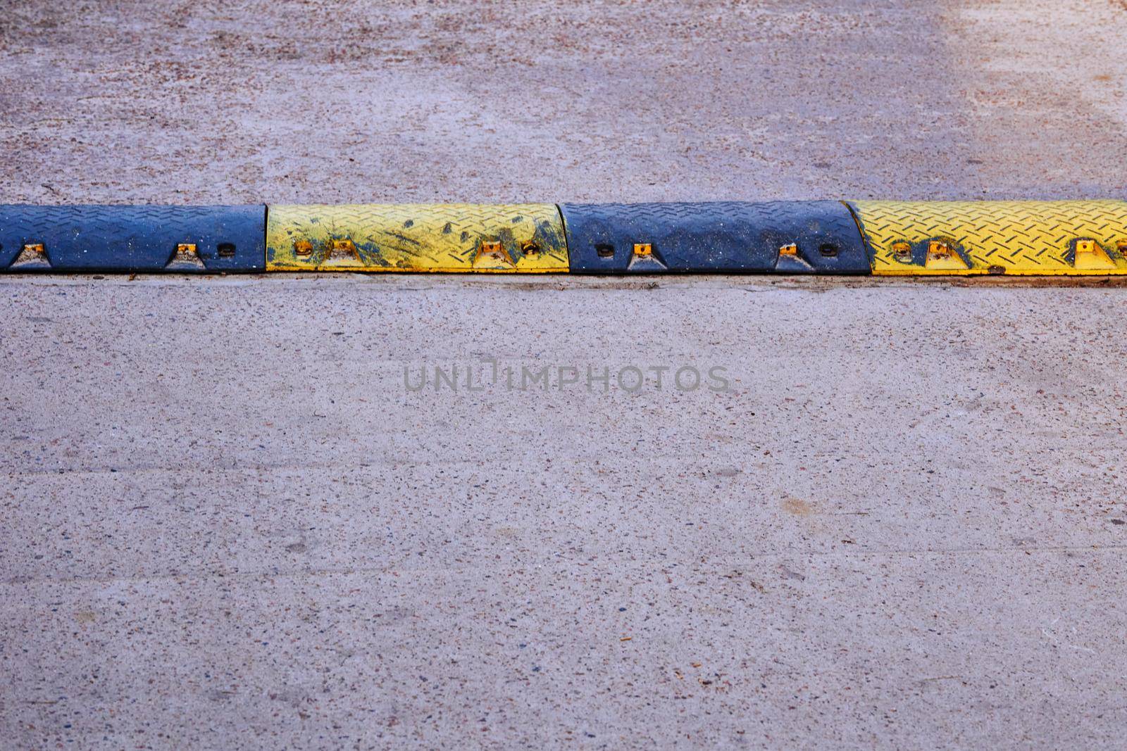 Black and yellow speed bump on chipped asphalt by jovani68