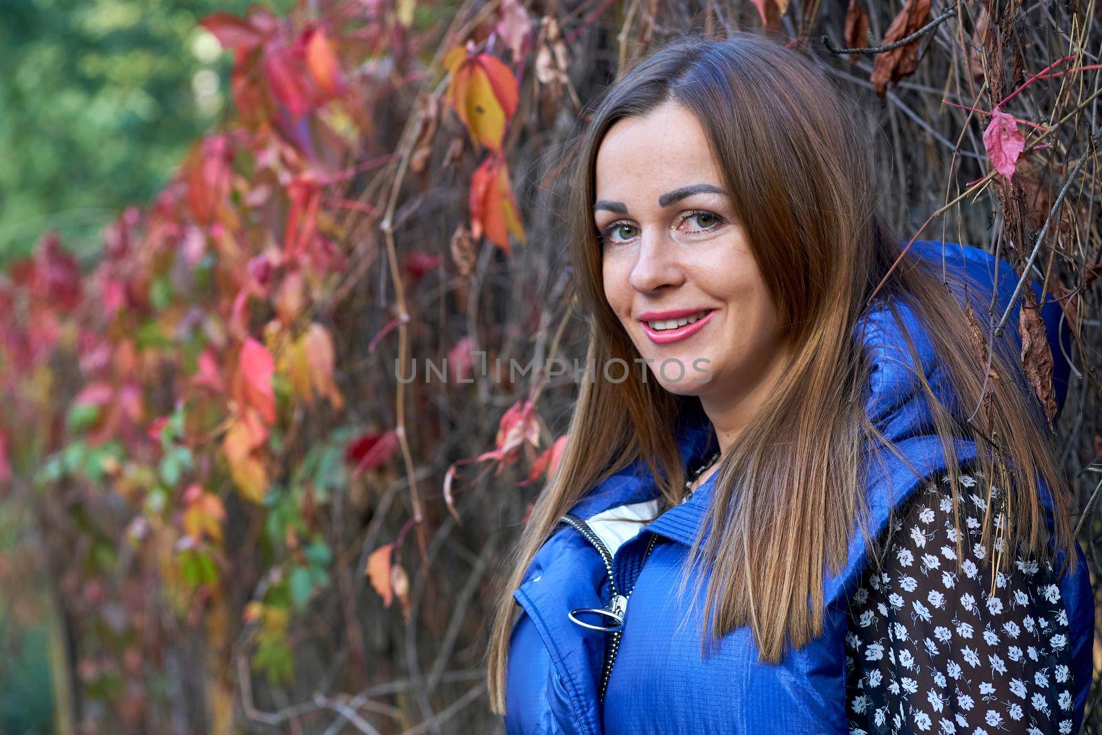 Cute smiling girl in a blue vest and red orange bushes by jovani68