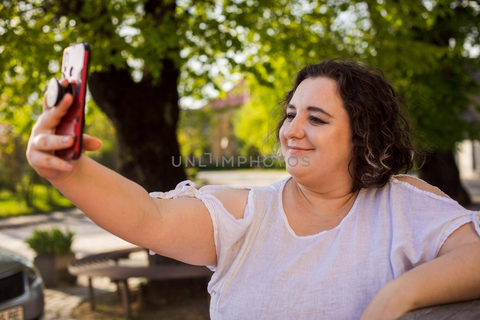 Smiling woman at outdoors cafe using mobile and having video call.