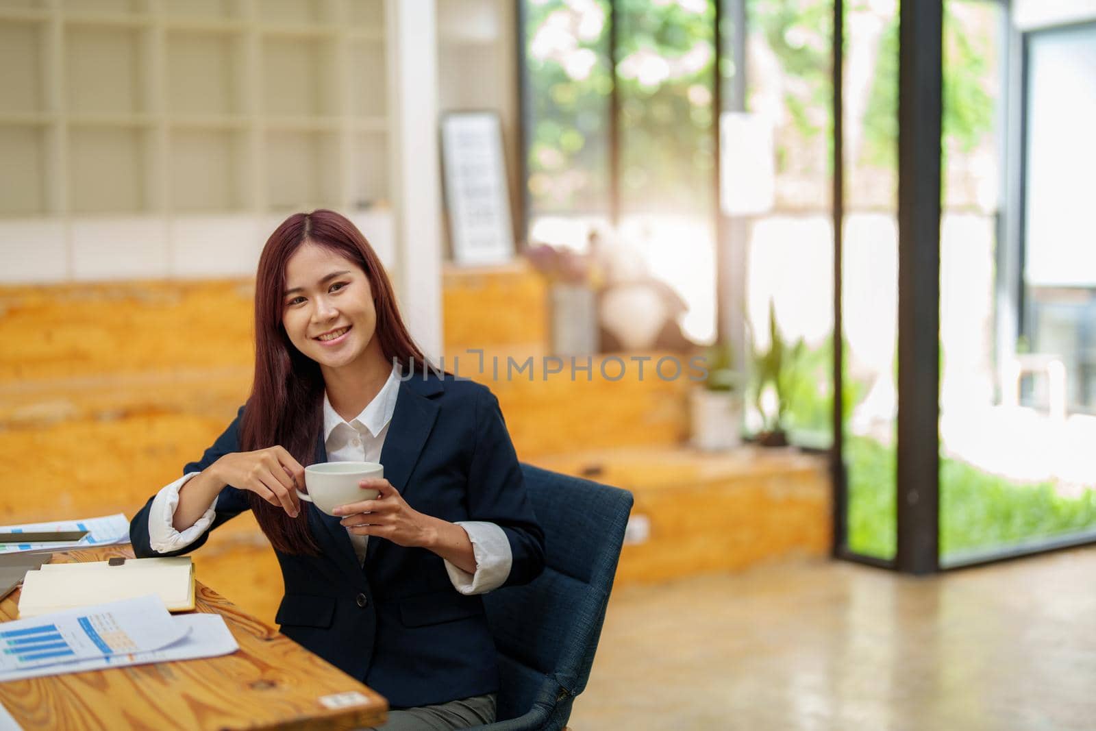 Asian female worker using computer and budget documents on desk.