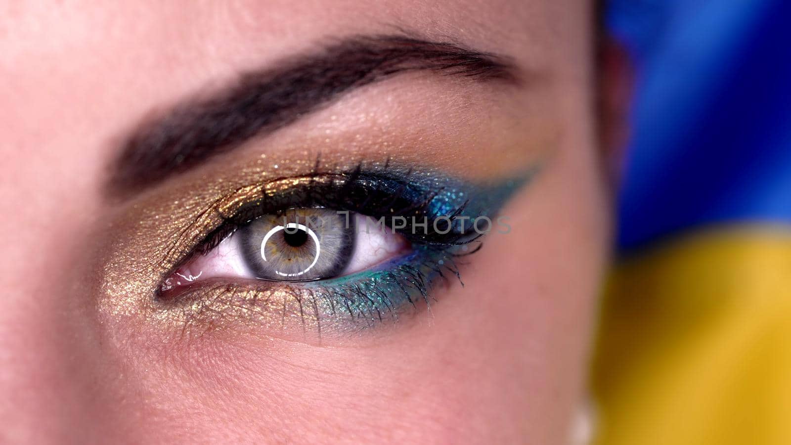 Macro view of woman eye with blue yellow shiny make-up. Lady, green cornea with round reflection. Ukrainian model on flag background. High quality 4k footage