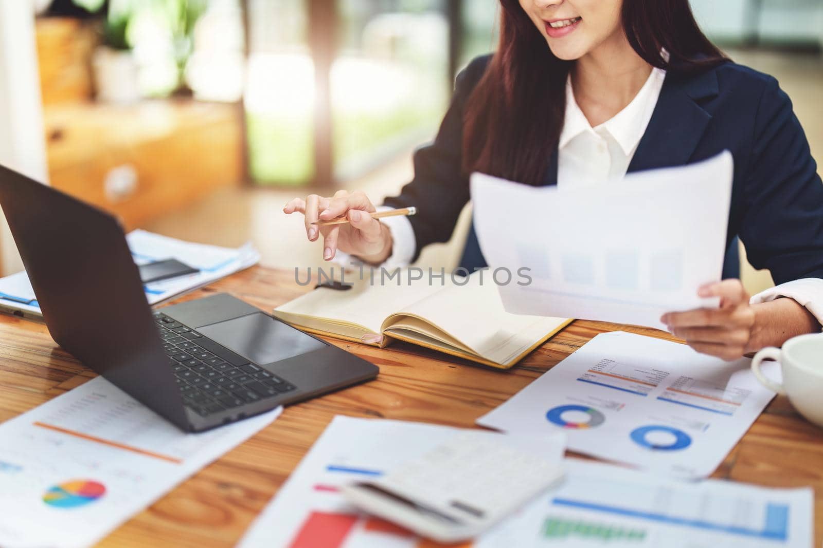 Asian female worker using computer and budget documents on desk.