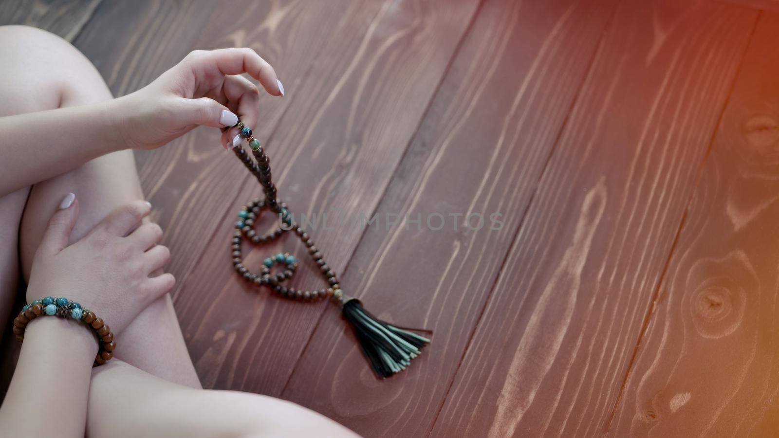 Woman lit hand counts mala beads strands of gemstones used for keeping count during mantra meditations. Lady sits on wooden floor. Spirituality, religion, God concept. Copy space by kristina_kokhanova