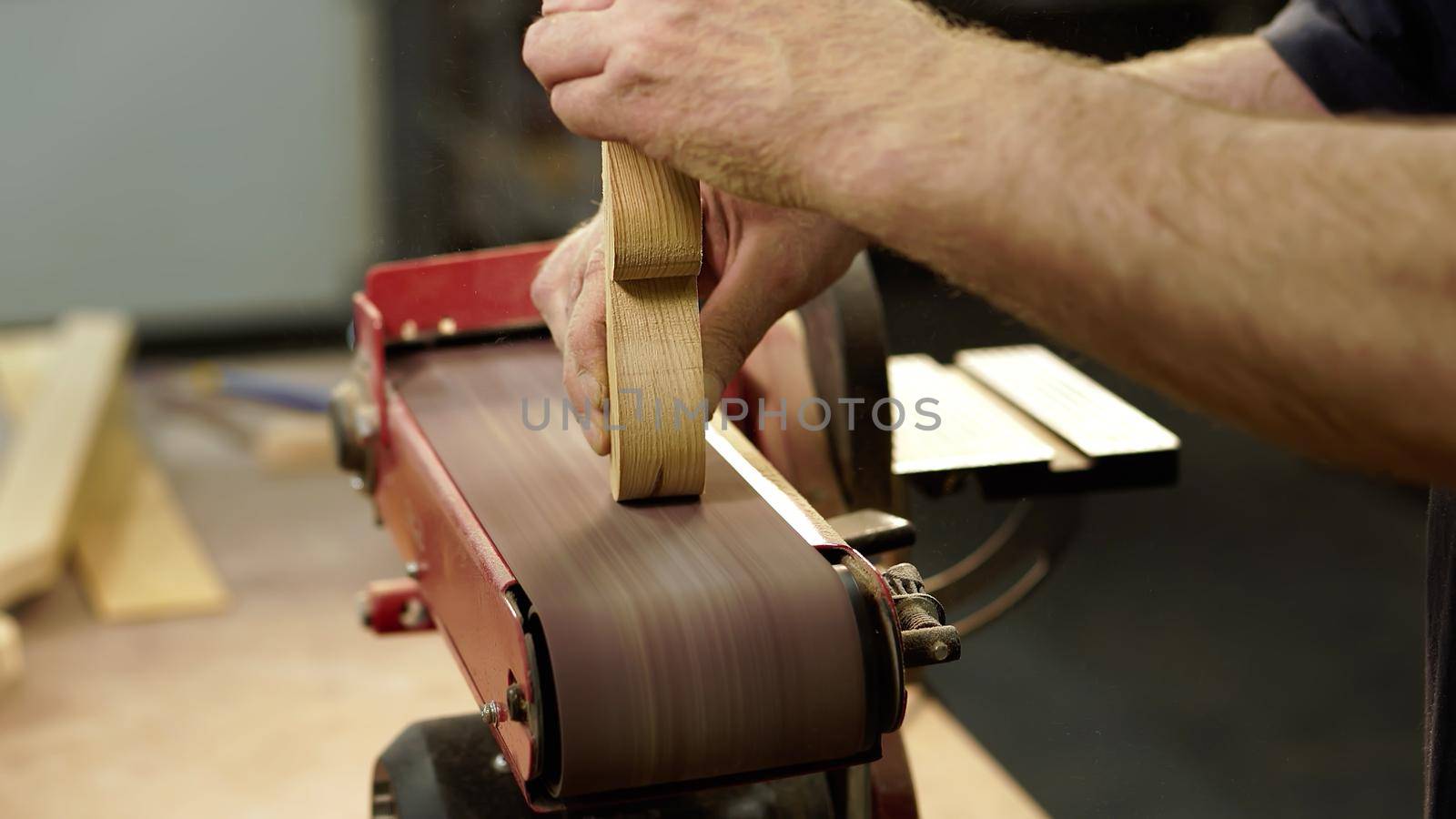 Hands of carpenter sharpens wooden part on grinding machine. Handwork concept, woodworking workshop. High quality photo