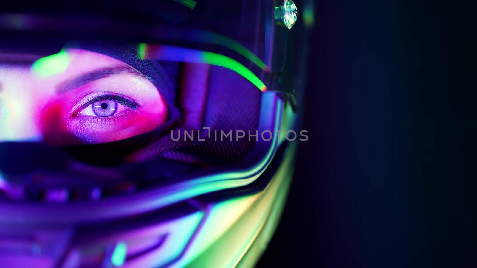 Young female motorcyclist woman in closed motorcycle helmet. Driver biker looking to camera under colorful neon light. Amazing aesthetic portrait. High quality photo