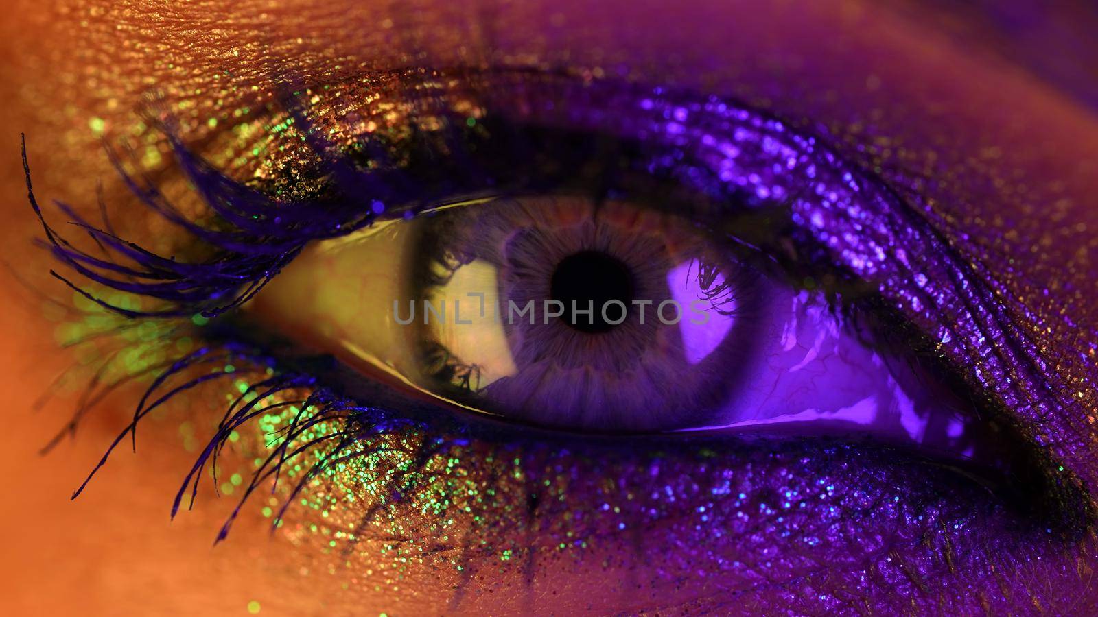 Close-up of woman eye under neon light. Female with beautiful makeup, glitter shadows. Beauty, cosmetics, night club lifestyle concept. High quality photo