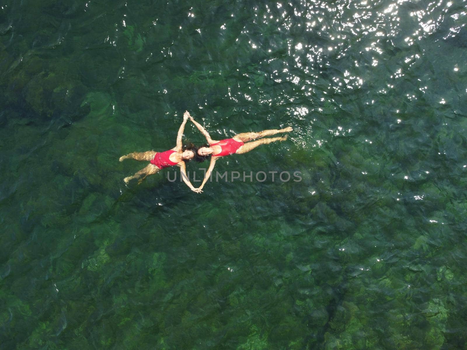 Woman floating sea. Aerial top view of two pretty woman in red swimsuit floating on water surface in crystal clear turquoise sea. Vacation at Paradise. Ocean relax, travel and vacation. Slow motion by panophotograph