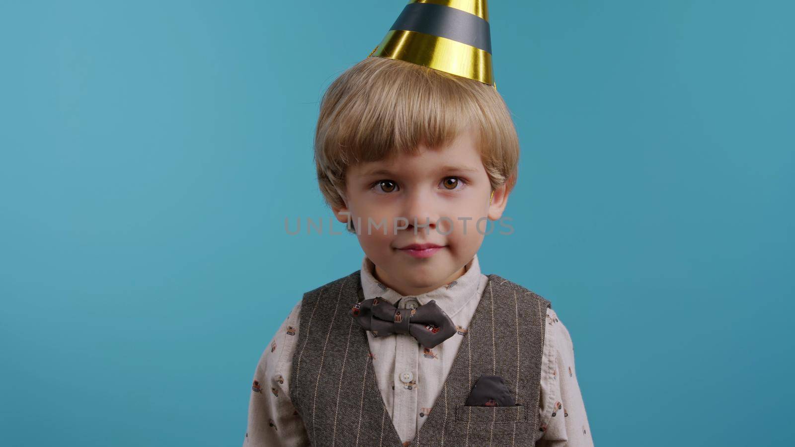 Smiling little birthday boy in cone hat on blue wall background. Happy emotional child. Amazement in eyes, happy childhood. High quality photo